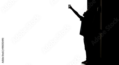 A silhouette of a person standing in a doorway holding a phone up in the air.