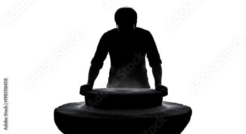 A silhouette of a man standing behind a large stone mortar and pestle