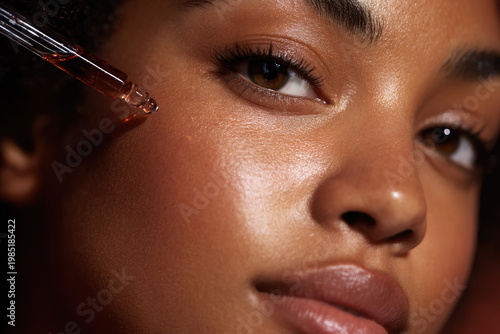 Beautiful black woman applying face serum with a dropper