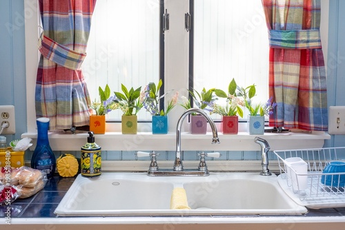 Modern farmhouse kitchen sink with colorful planters and plaid window curtains