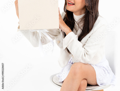 Asian woman body in white short skirt sitting on chair holding plain gift box, isolated on white background