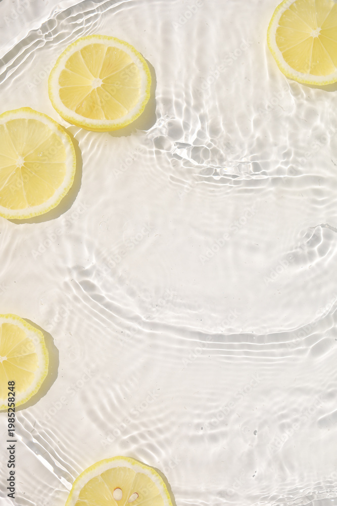 Obraz premium Fresh yellow lemon slices floating in clear water with ripples texture.