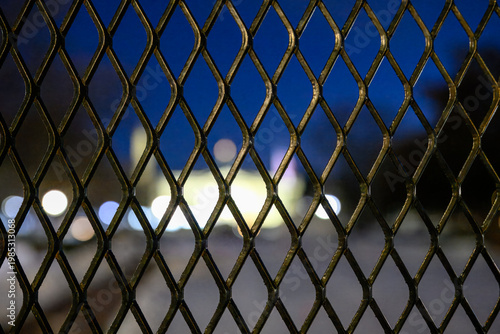View of a building through a wire fence at night with blurred lights creating a unique scene