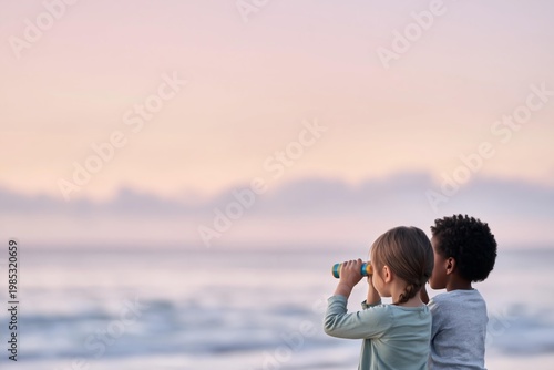 Two children looking through binoculars at the ocean during sunset