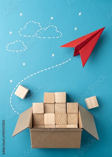 Red paper airplane flying out of cardboard box with wooden blocks and clouds image