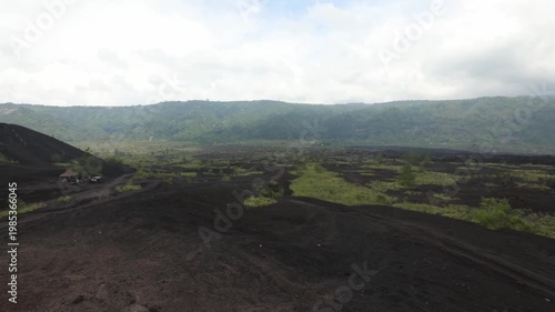 A cinematic ground-level shot pans slowly to the left across the rugged and desolate black lava fields at the base of Mount Batur