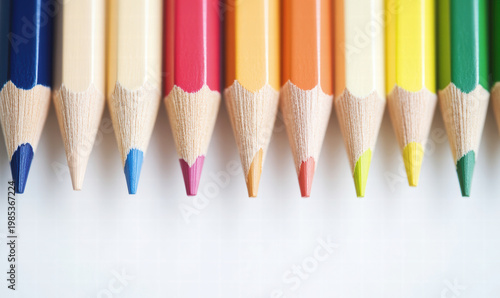 Brightly colored pencils lined up neatly with sharp tips pointing down on plain 