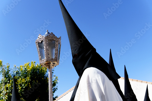 Nazareno figure dressed in traditional Pointed hood and robe carrying an ornate lantern while participating in a religious holy week street procession in spain