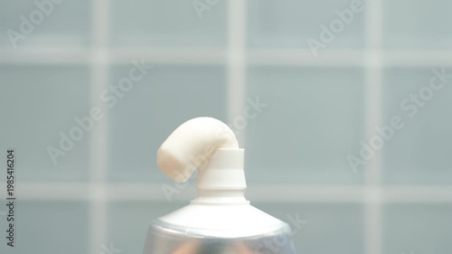 Squeezing toothpaste from tube against a blue bathroom tile background.