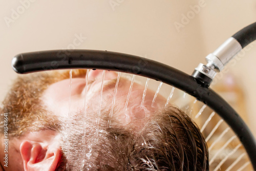 Close-up of Bearded Man receiving a head massage during a Japanese head spa treatment with water flowing from a special hair washing tool, focusing on the scalp relaxation and beauty therapy	