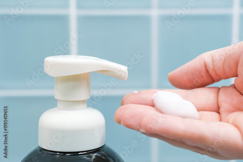 Female hand squeezing soap foam from black dispenser on blue background.