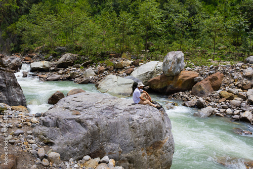 Canvas Print A serene woman sitting on a large rock by a river in Madhyamaheshwar temple, Utt