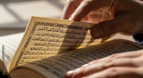 A person's hands carefully turn the pages of an open book, revealing Arabic script.