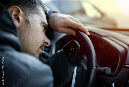 Man sitting in car at gas station during fuel crisis,checking empty wallet and holding payment card.Concept of rising fuel prices.Driver leaning on steering wheel.Close of fuel nozzle into car tank.