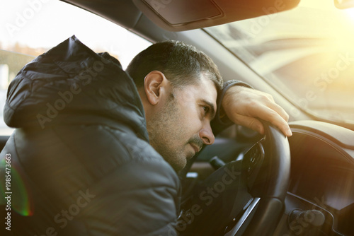 Man sitting in car at gas station during fuel crisis,checking empty wallet and holding payment card.Concept of rising fuel prices.Driver leaning on steering wheel.Close of fuel nozzle into car tank.