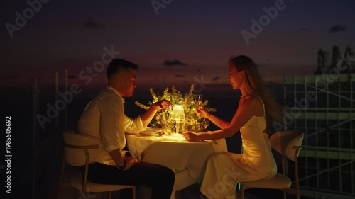 Romantic couple enjoying a candlelight dinner at sunset, laughing together as the wind gently blows the womans hair in a beautiful evening atmosphere