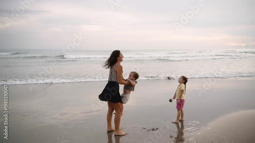 Family having fun together on the beach at sunset, enjoying quality time by the ocean. Warm pink light, joyful atmosphere, and carefree moments of vacation, childhood. Mother, daughter and son 