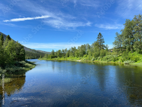 Serene river flowing through lush green Scandinavian landscape under a blue sky
