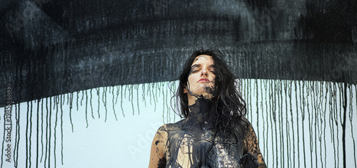 Portrait, hands and torso of a naked sensual woman full of feeling, emotion in black color painted in front of Studio wall with dripping paint. Decorative abstract body painting art