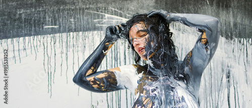 Sexy nude woman covered in abstract black, white, and gold paint, standing against a dripping, textured backdrop, embodying a fusion of art and human form