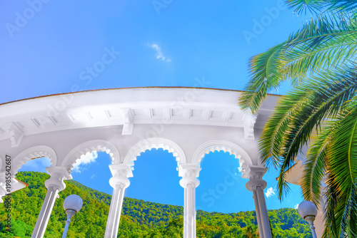 Famous white Gagra Colonnade landmark in Abkhazia with palm trees and mountains.