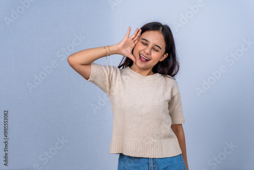 Quadro su tela Playful Asian woman in beige shirt making a funny face and gesturing on grey bac