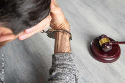 Man in handcuffs with a judge gavel on the table.