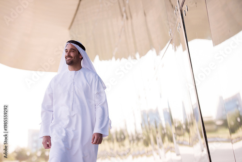 Tableau sur toile Smiling man in traditional Middle Eastern thobe walking beside reflective modern