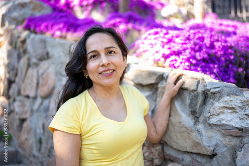 Woman smiling, enjoying a pleasant day outdoors during travel, leaning on a stone wall with flowers