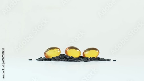 Golden black sesame oil softgel capsules on a pile of raw black sesame seeds
