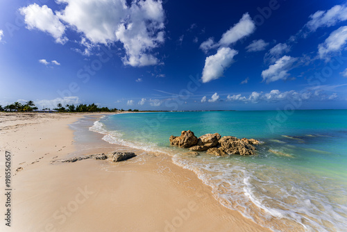 Crystal-clear turquoise water gently washing over a sandy beach with rocks and soft waves in Treasure Cay, Great Abaco, Bahamas - an idyllic Caribbean coastline
