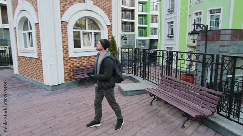 Stylish Young Man in Winter Clothing Walking Through a Modern Urban Residential Courtyard