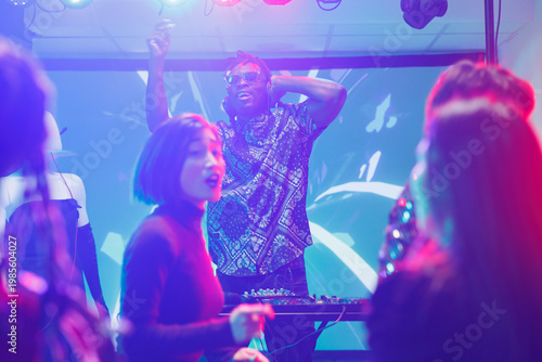 Fotografie People partying on dancefloor while young dj performing on stage in nightclub