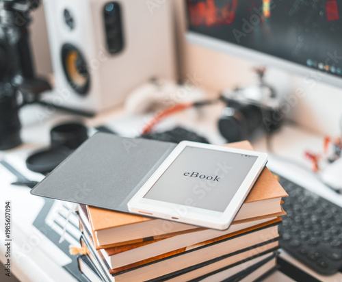 Ebook reader placed on stack of books in modern workspace. Digital device contrasts with printed literature, representing blend of technology and traditional reading in creative and productive 