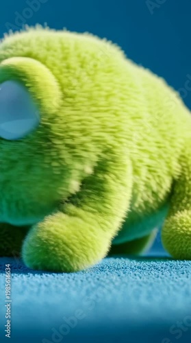 Close-up of a green stuffed frog toy with big eyes on a blue surface against a blue background.