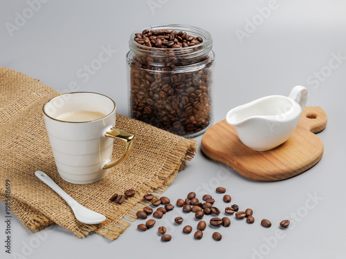 Cup of coffee, a glass can with roasted coffee beans and a cream sauceboat.