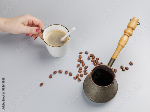 Cezve with roasted coffee beans and a woman's hand with a cup of coffee.