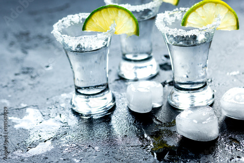 Tequila shot with lime slices and salt on dark background
