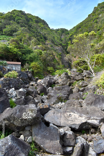 Stone house on the hillside set in a lush green valley with a rocky stream bed
