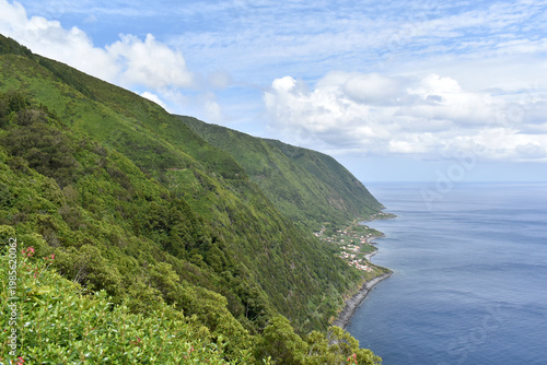 View of forested steep slopes with a small village on the coast, ocean waves, Sao Jorge Island, Azores