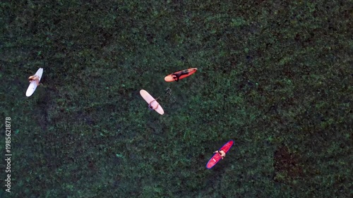 Surfers waiting on surfboards in clear ocean water. Great aerial view drone