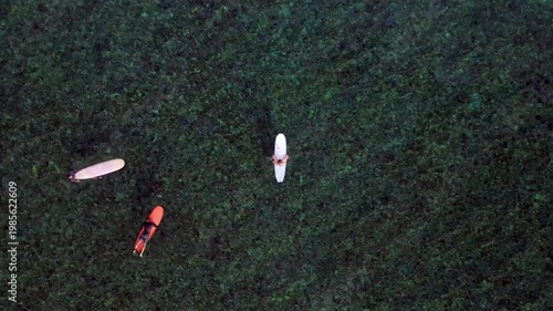 Surfers waiting on surfboards in clear ocean water. Nice aerial view drone
