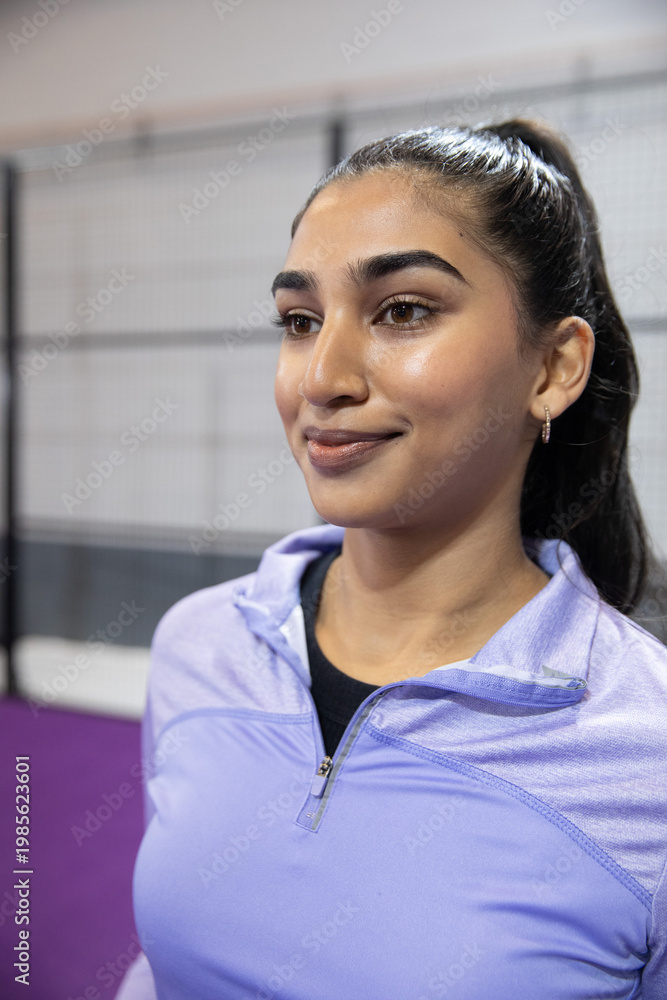 Obraz premium Indian adult woman standing and posing in sports facility with purple court and quarter-zip top