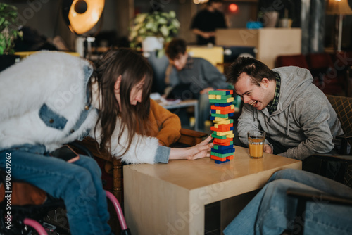 Students with disabilities and friends laugh and play a colorful stacking block game at a table. A group of young people enjoy a relaxed, inclusive game session in a casual cafe setting.