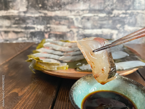 Fotografie サワラとアオリイカの昆布締め。新鮮な刺身を昆布で包んで熟成させた料理。サワラに醤油をつけて食べるところ。