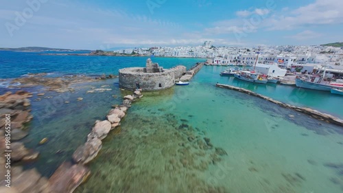 A smooth FPV drone flight over Naousa village on Paros island, Greece, showcasing whitewashed buildings, narrow streets and coastal harbor in bright daylight