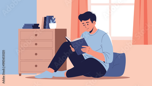 Relaxed young man sitting comfortably on the floor of a cozy living room while focused on reading an interesting book near a dresser.