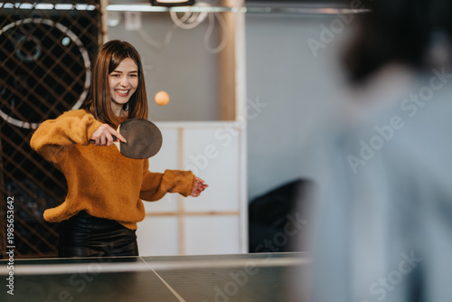Foto A female student serves a ping pong ball across a table while smiling