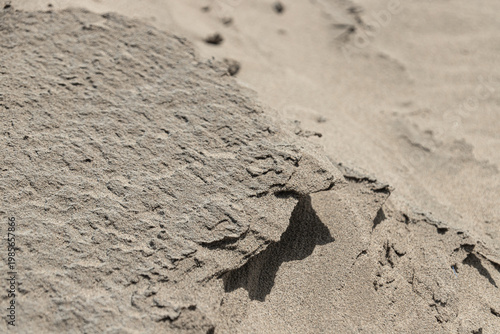 Closeup textured wet sand formation on a beach, showing a naturally eroded ridge with a sharp edge casting a defined shadow on the surrounding dry sand.