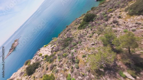Dynamic FPV drone flight over a field of yellow flowers transitioning into rocky coastal cliffs with a scenic lighthouse reveal at the end